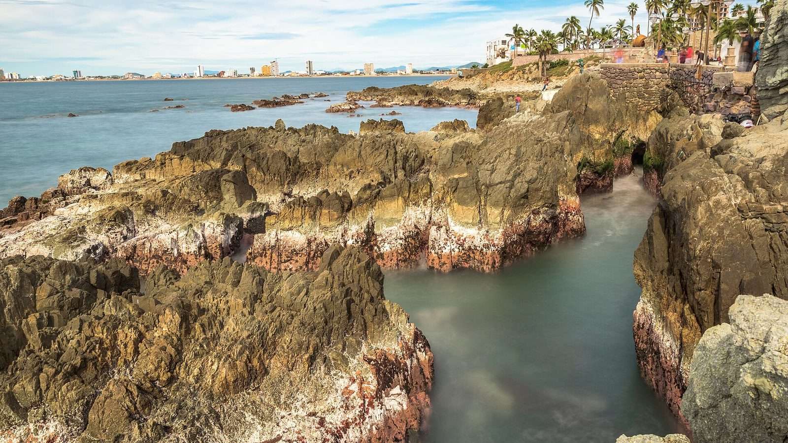Rocky shoreline in Mazatlán, with the Golden Zone skyline across the bay